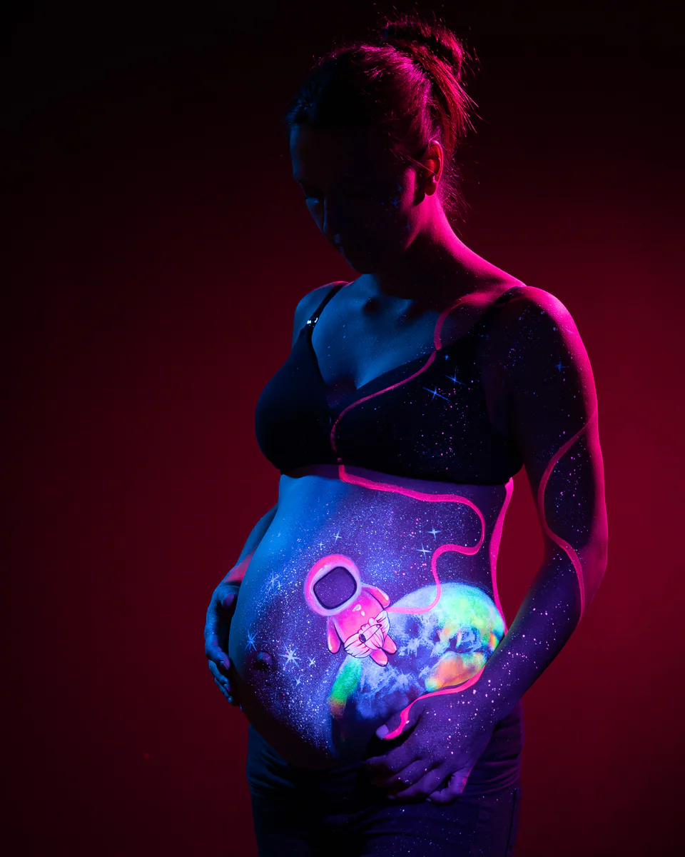 Babybauch mit Astronautenmotiv im Schwarzlicht