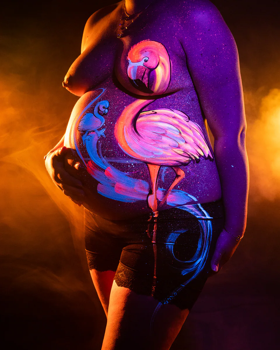 Babybauch mit gemaltem Flamingomotiv unter farbigem Licht