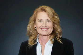 Smiling woman with wavy blonde hair, a black blazer and a light blue blouse