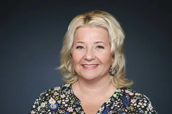 Smiling woman with blonde hair and a floral blouse against a dark background