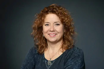 Smiling woman with reddish curls, a dark top and a necklace