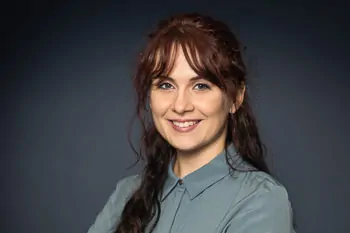 Smiling woman with dark hair and a grey-blue blouse against a dark background