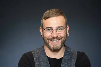 Smiling man with glasses, a beard, a black top and a grey waistcoat