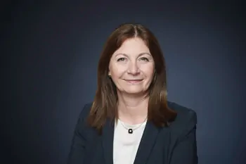 Woman with brown hair, a dark blazer and a white top against a blue background