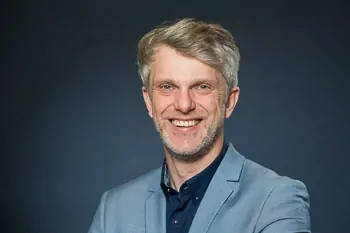 Smiling man with grey hair and a light blue jacket against a dark background