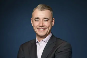 Smiling man with short grey hair, a dark jacket and a light shirt against a blue background