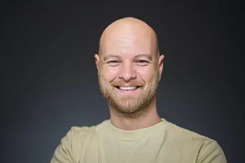 Smiling man with a short beard and a light T-shirt against a dark grey background