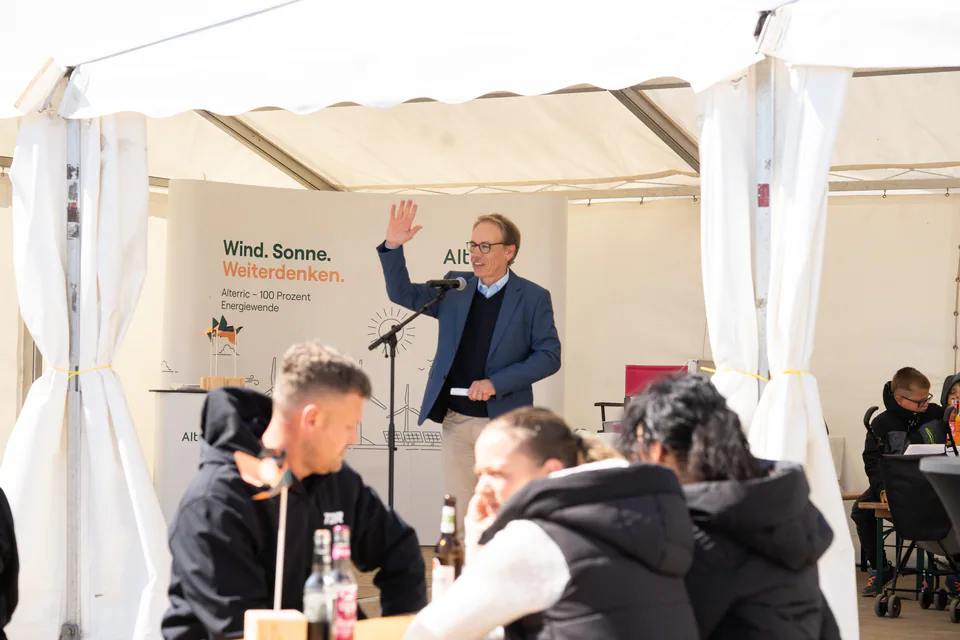Mann am Mikrofon vor Publikum unter einem Zelt