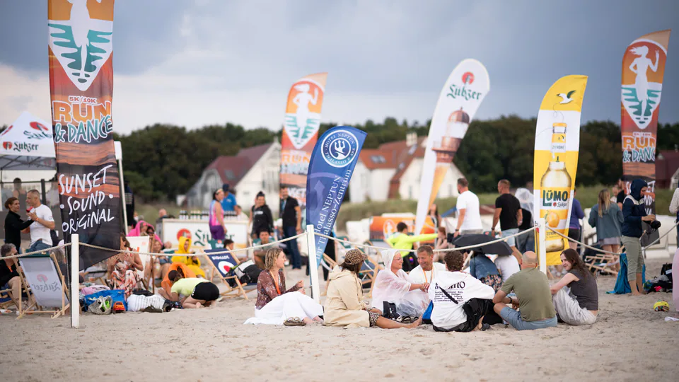 Menschen bei einer Veranstaltung am Strand zwischen Werbefahnen