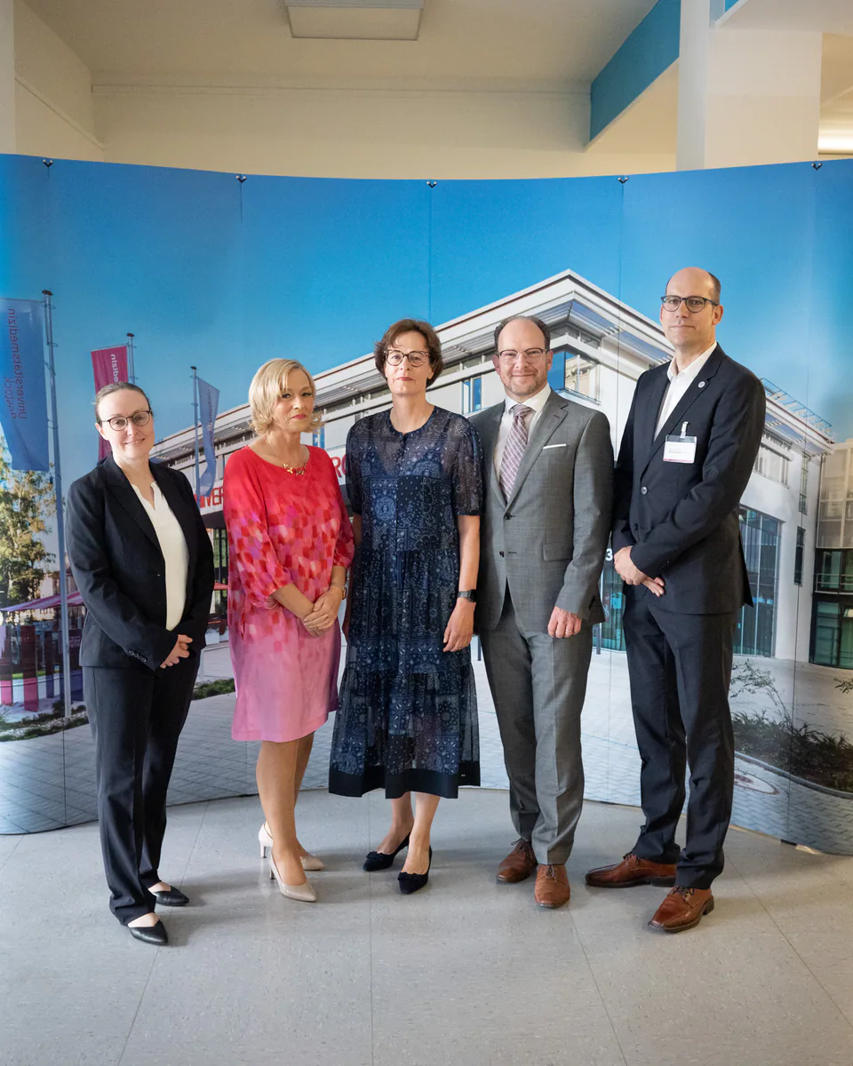 Five people in a group portrait in front of a building backdrop