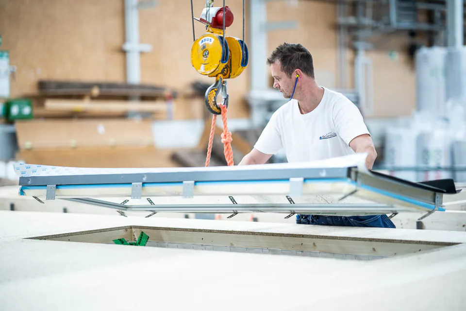 Mann in weißem T-Shirt arbeitet an einem Kran in einer Produktionshalle