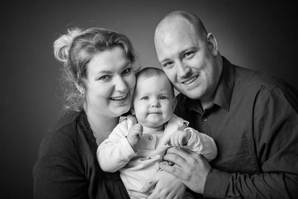 Schwarz-Weiß-Portrait eines Paares mit Baby vor dunklem Hintergrund.