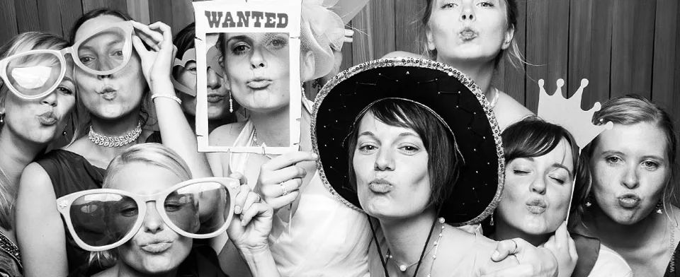 A group with hats, glasses and props in front of a Photo Booth
