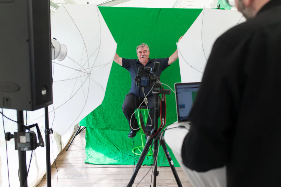 A photo studio setup with a green backdrop, camera and umbrella lights