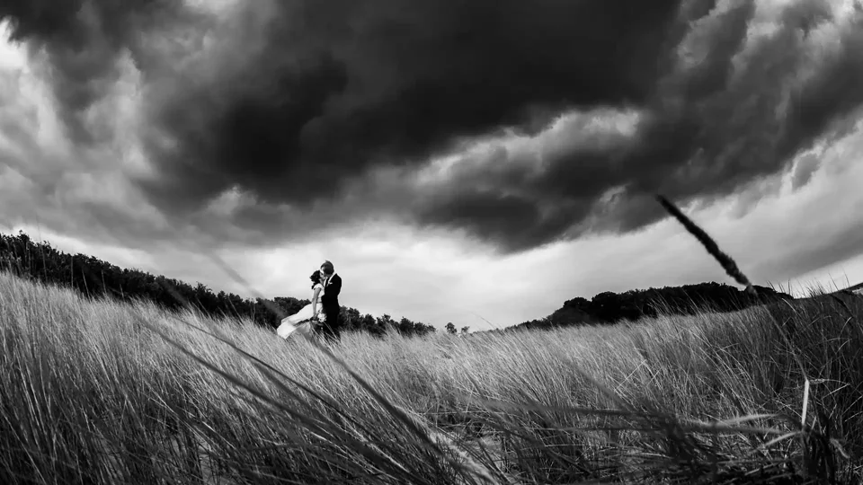Schwarz-Weiß-Hochzeitsfoto in den Dünen von Graal-Müritz unter dramatischen Wolken