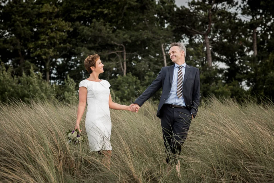 The bride and groom hold hands in the dunes on the beach in Zingst