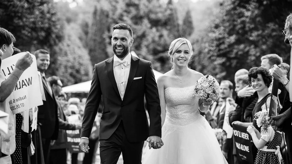 Black-and-white photo of a wedding couple walking hand in hand between guests