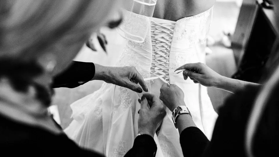 Mehrere Hände schnüren das Brautkleid am Rücken