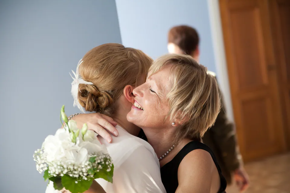 Eine Frau umarmt die Braut mit Blumenstrauß bei einer Hochzeit