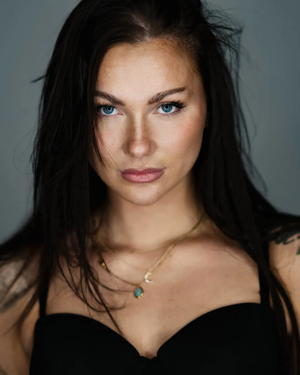 Nahes Portrait einer Frau mit dunklem Haar und blauen Augen vor grauem Hintergrund