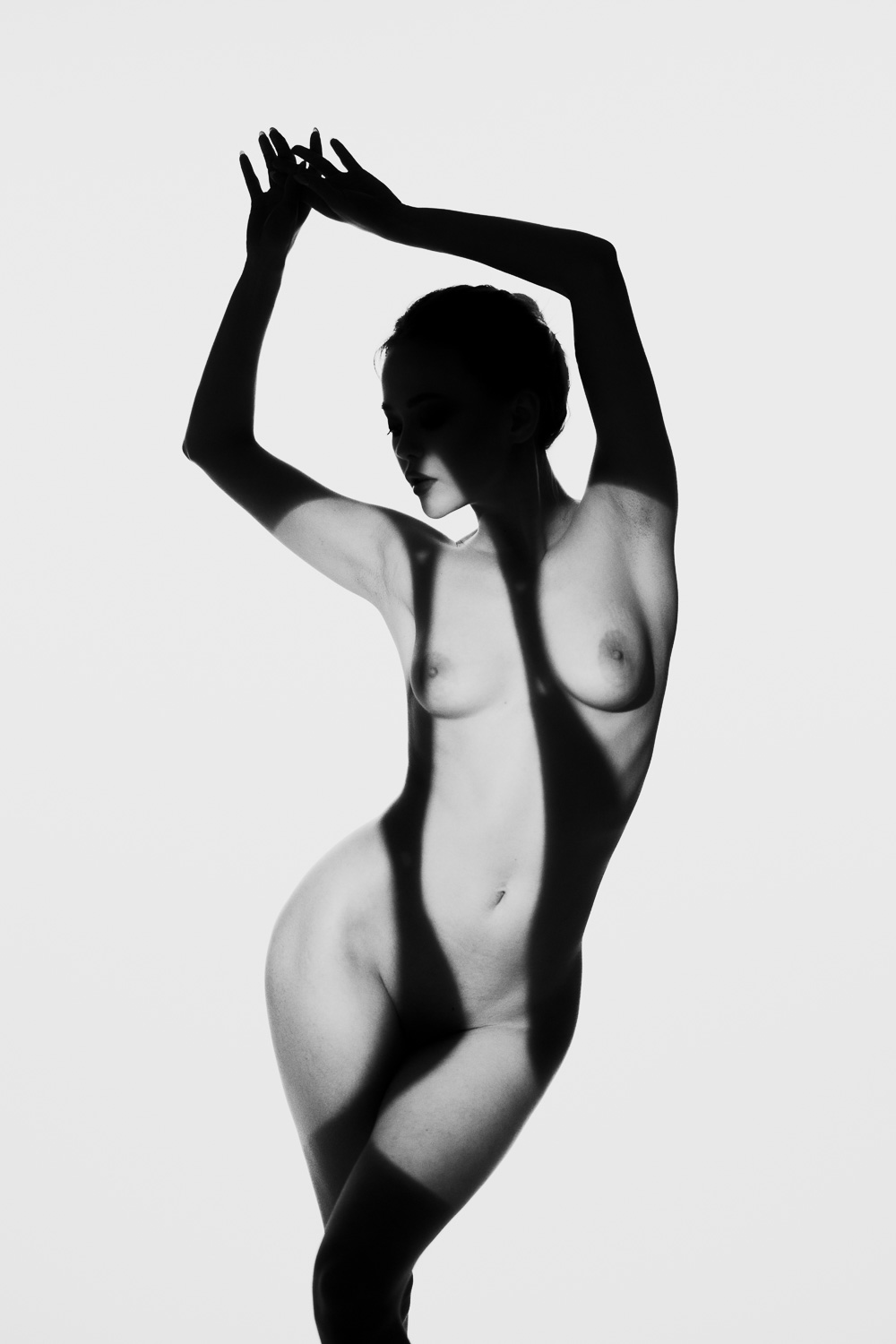 Eine kunstvolle Schwarz-Weiß-Fotografie einer Frau im Schatten und Licht. Die kunstvolle Beleuchtung und scharfe Schatten erzeugen eine faszinierende Atmosphäre.